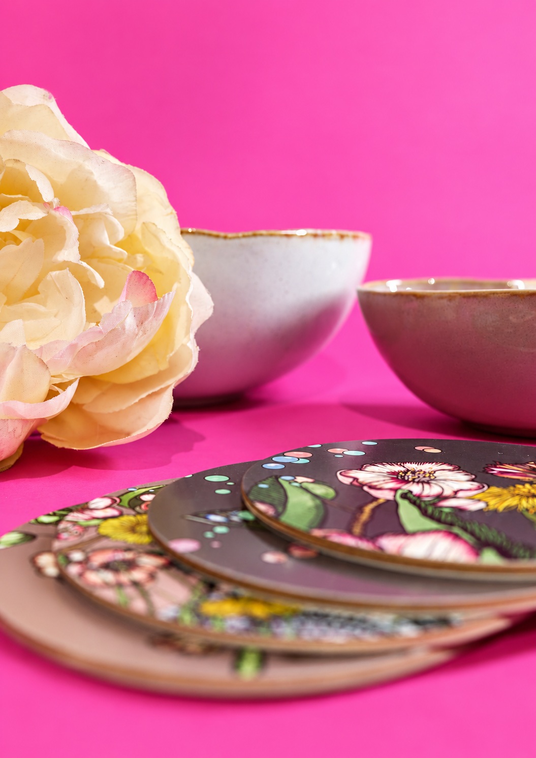 Un dialogue de couleurs — Le fond rose répond aux motifs de la vaisselle ; la fleur apporte une autre texture et prolonge le thème floral.