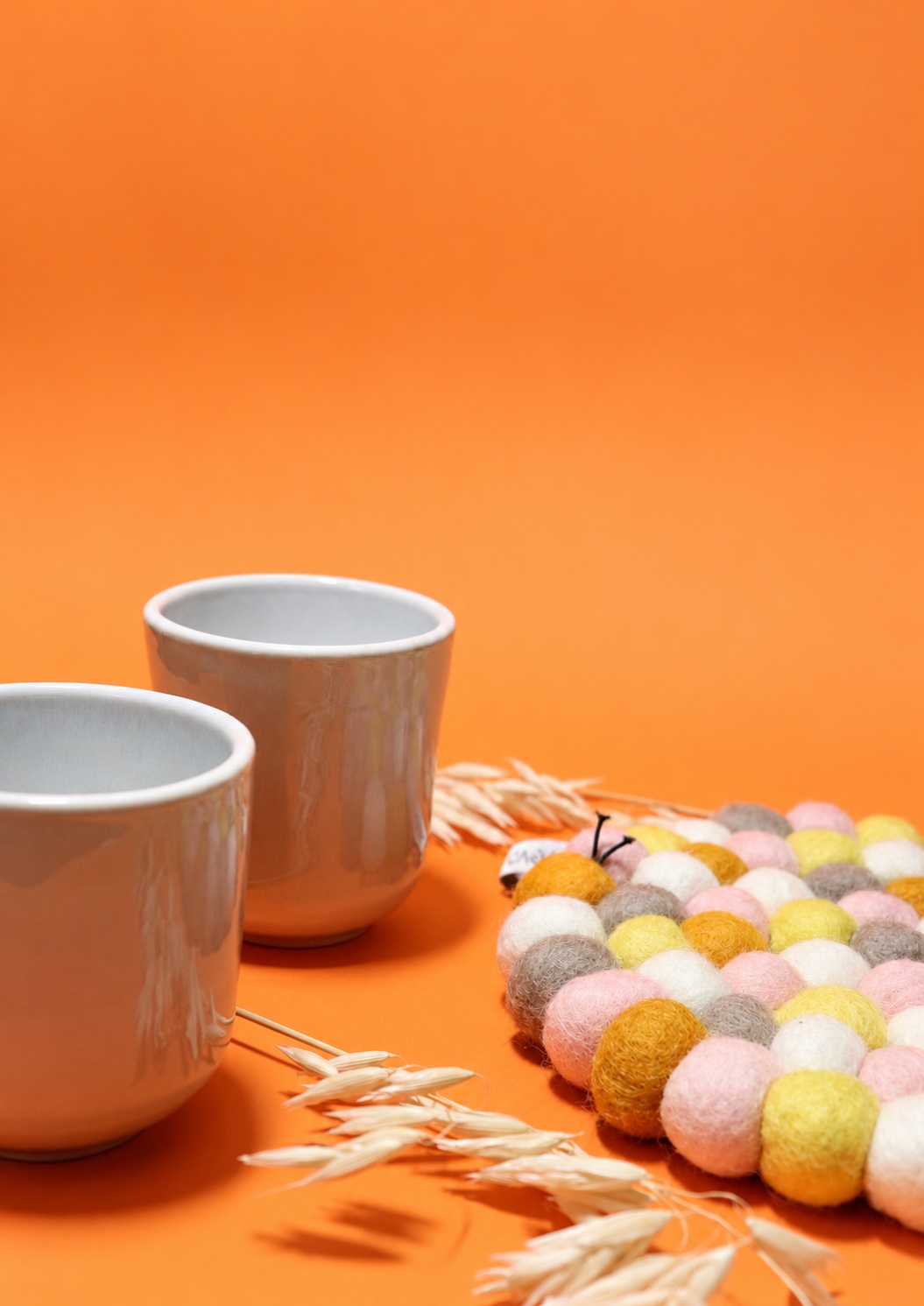Matières et contrastes — Le fond orange fait ressortir la céramique et les nuances pastel du feutre. Les éléments végétaux relient les objets dans la composition.